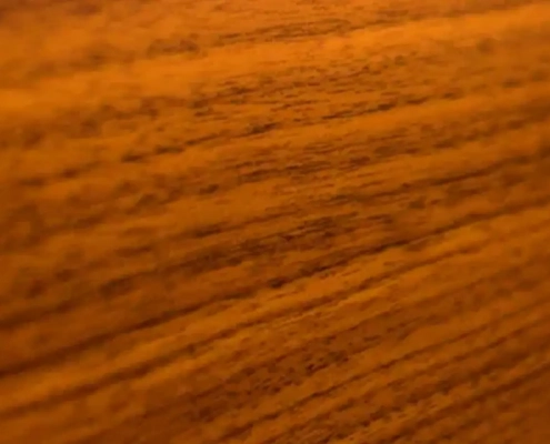 Detailaufnahme einer warmen, goldbraunen Teakholz-Oberfläche mit feiner Holzmaserung.