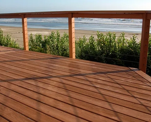 Großzügige Holzterrasse mit Geländer und freiem Blick auf den Strand und das Meer.