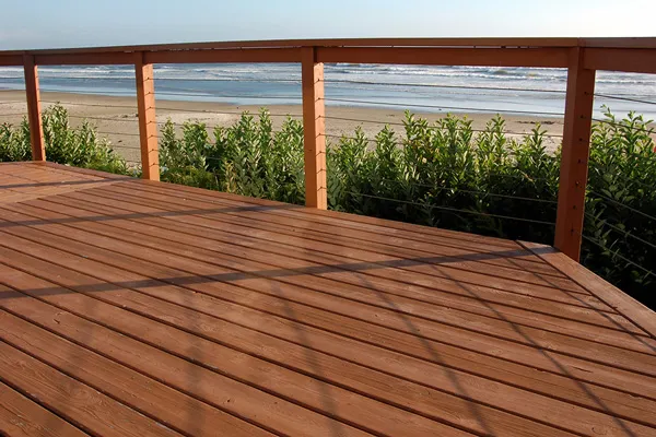 Großzügige Holzterrasse mit Geländer und freiem Blick auf den Strand und das Meer.