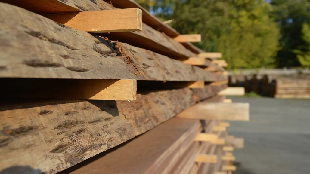 Gestapelte Unbesäumte Holzbohlen (Blockware) mit Stapelhölzern zur Trocknung auf dem Holzplatz.