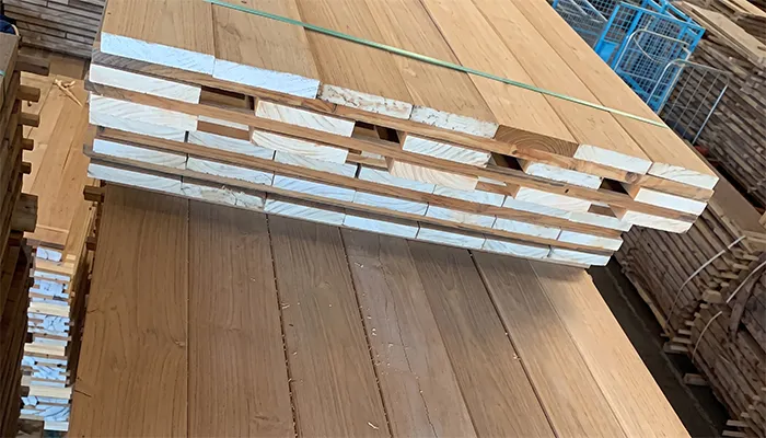 Zertifiziertes Teak-Schnittholz Gestapelte Bretter aus zertifiziertem Teak-Schnittholz auf einer Palette in einer Lagerhalle