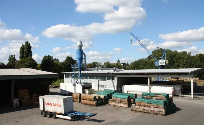 Vogelperspektive auf das WOB Timber Freilager mit Holzstapeln und Lagerhallen.