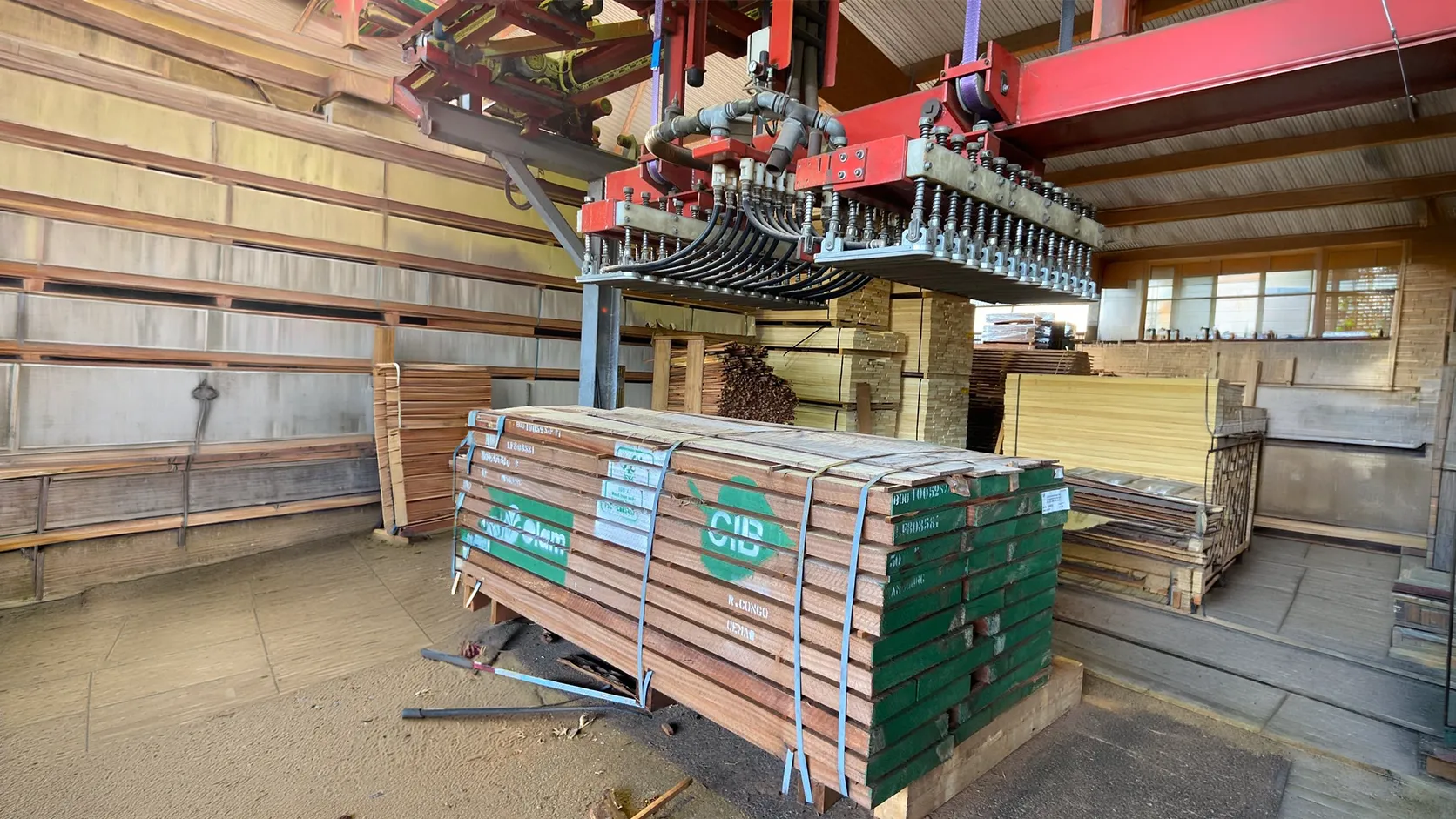 Industrieller Vakuumheber beim Transport und Verladen von Holzpaketen in der Lagerhalle.