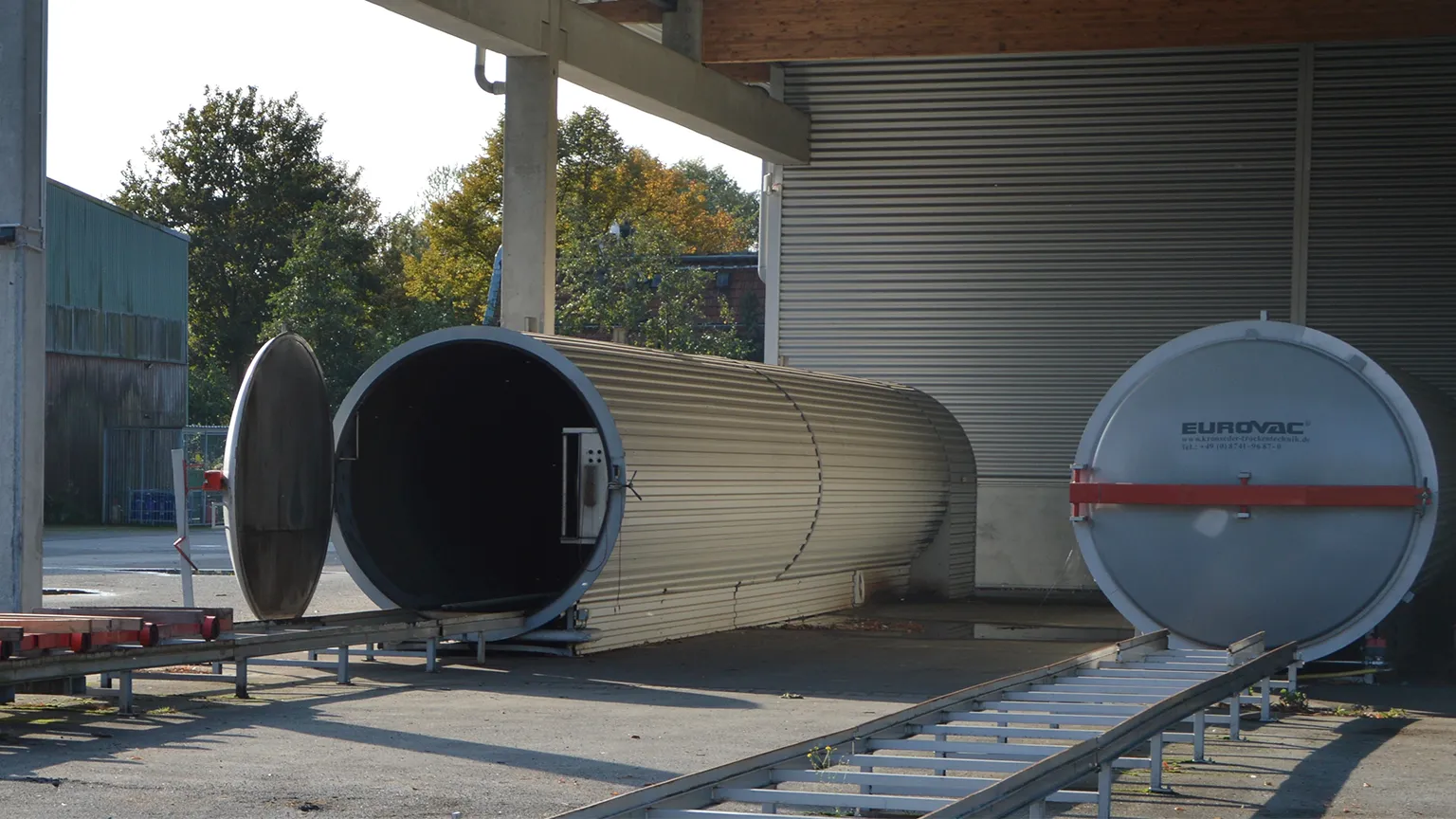 Moderne Vakuum-Trockenkammern (Eurovac) mit Schienensystem zur kontrollierten Holztrocknung im Außenbereich.